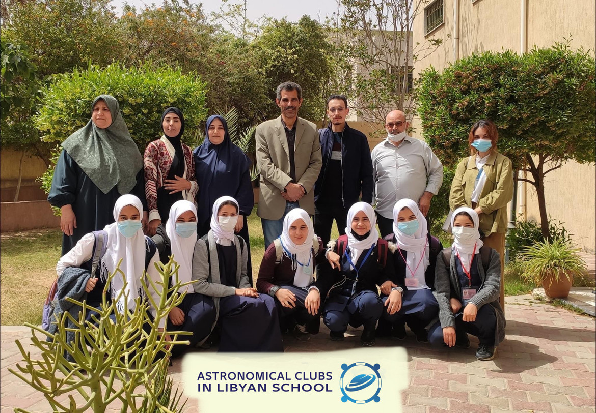 Eleven female and three male members of the Astronomical Clubs in Libya pose for a picture outdoors by trees and plants. The females are wearing head coverings.